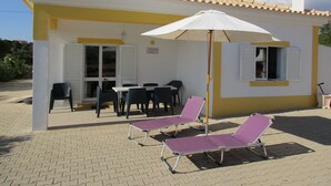 Ein Gebäude mit einem Ziegeldach, einer Außenbestuhlung mit Stühlen und Tischen sowie einer überdachten Terrasse mit Sonnenschirmen.