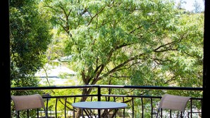 A balcony with two chairs and a small table, overlooking a parking area and trees. - Riverpark-studio apartment (Highgate Hill)