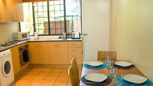 A compact kitchen with a washing machine, microwave, and a dining table set with plates and glasses. - Riverpark-studio apartment (Highgate Hill)