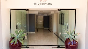 A hotel entrance with a glass door, a sign reading "RIVERPARK", and two large potted plants. - Riverpark-studio apartment (Highgate Hill)