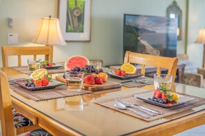 A dining table set with placemats, plates, cutlery, and a variety of fresh fruits and a glass of water. - *Island Sands 512* Maui Spacious Prime Oceanfront! SPLIT A/C! Amazing Views. (Wailuku)