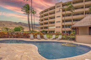 A hotel with a swimming pool, palm trees, and a view of mountains. - *Island Sands 512* Maui Spacious Prime Oceanfront! SPLIT A/C! Amazing Views. (Wailuku)