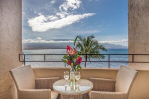 A balcony with wicker furniture, a glass table, a bottle of wine, and a vase of flowers.