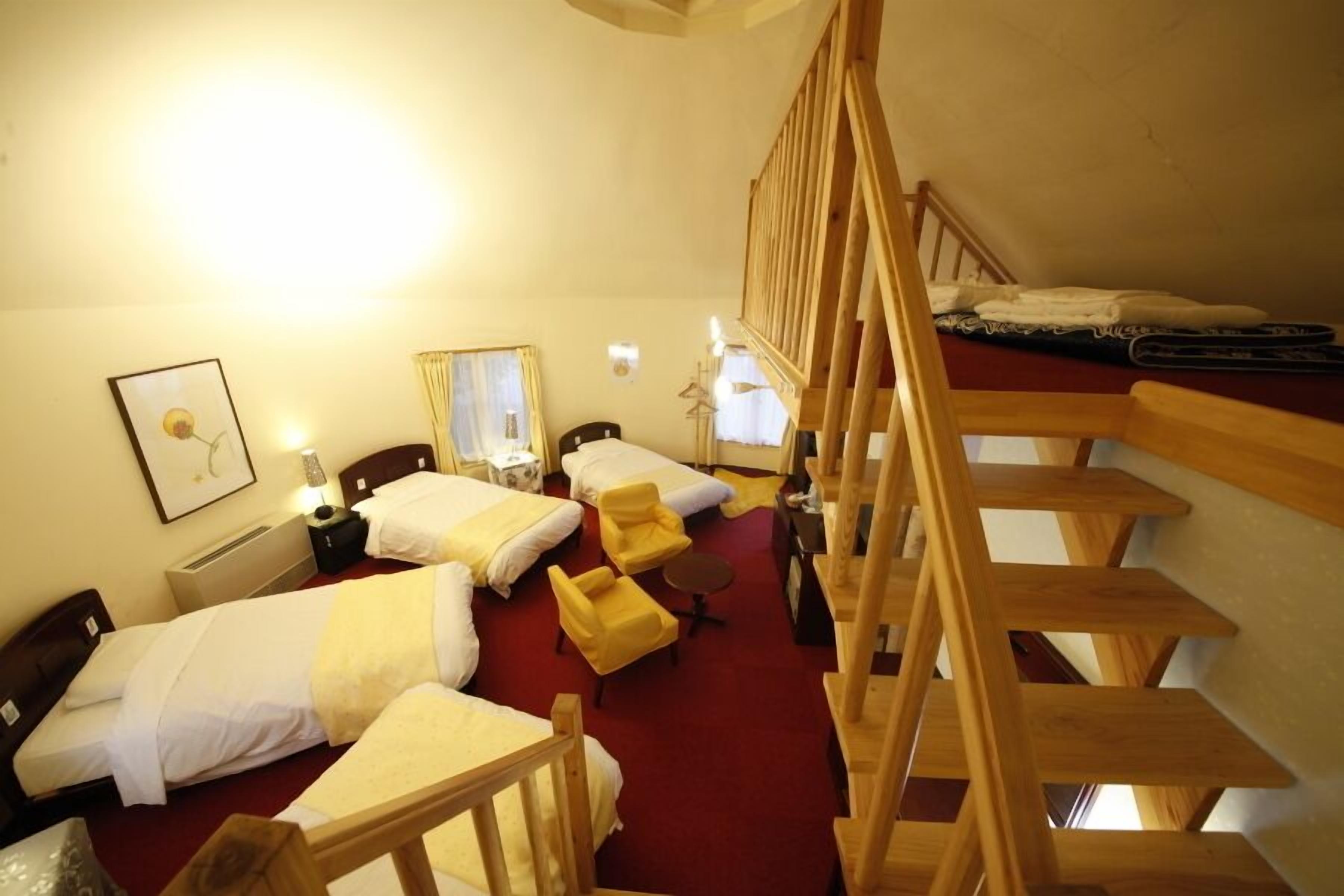 A hotel room with two beds, a wooden staircase, a red carpet, and a small table with a lamp.