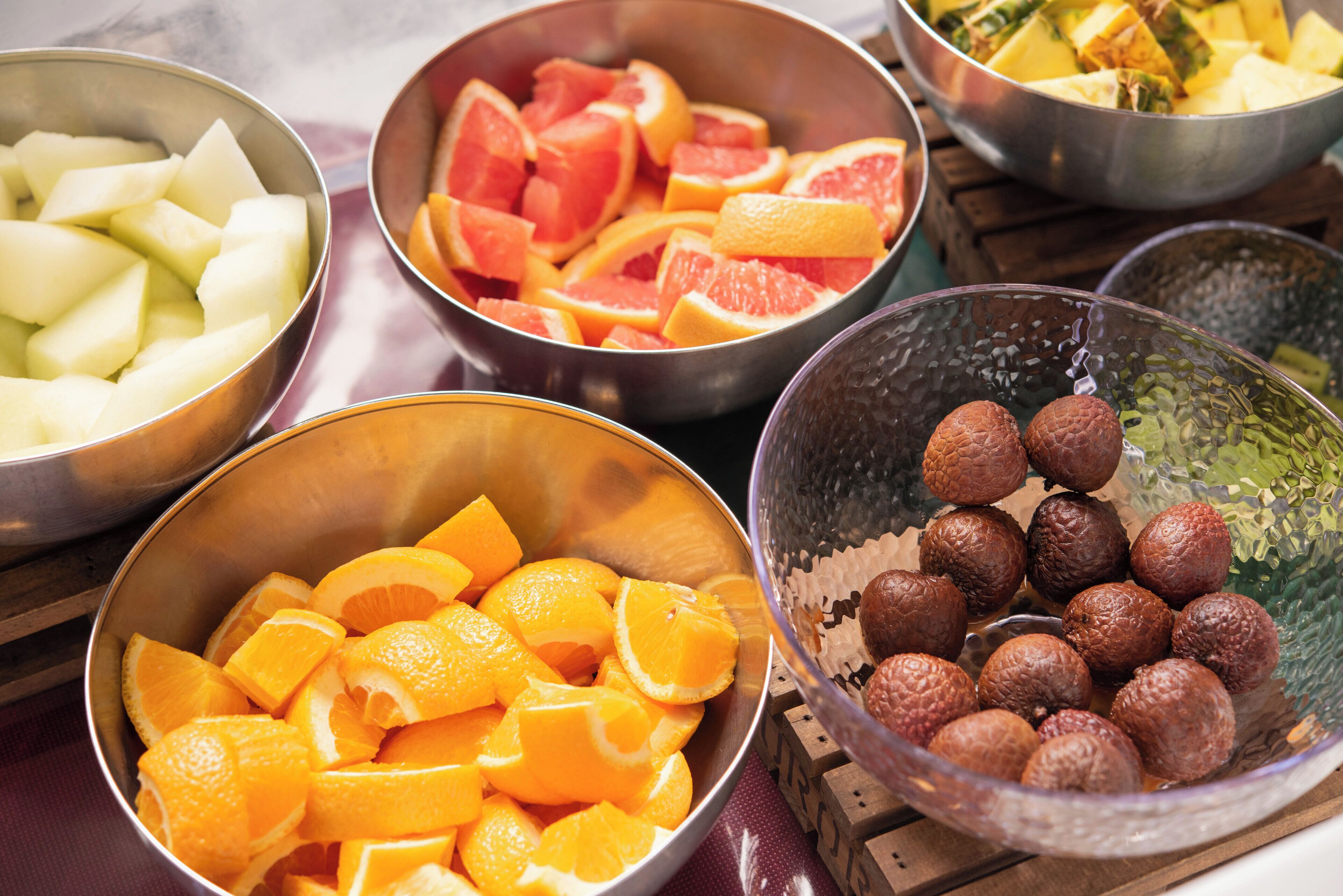 Verschiedene Früchte, darunter Orangen, Grapefruits und Äpfel, in Metallschüsseln.