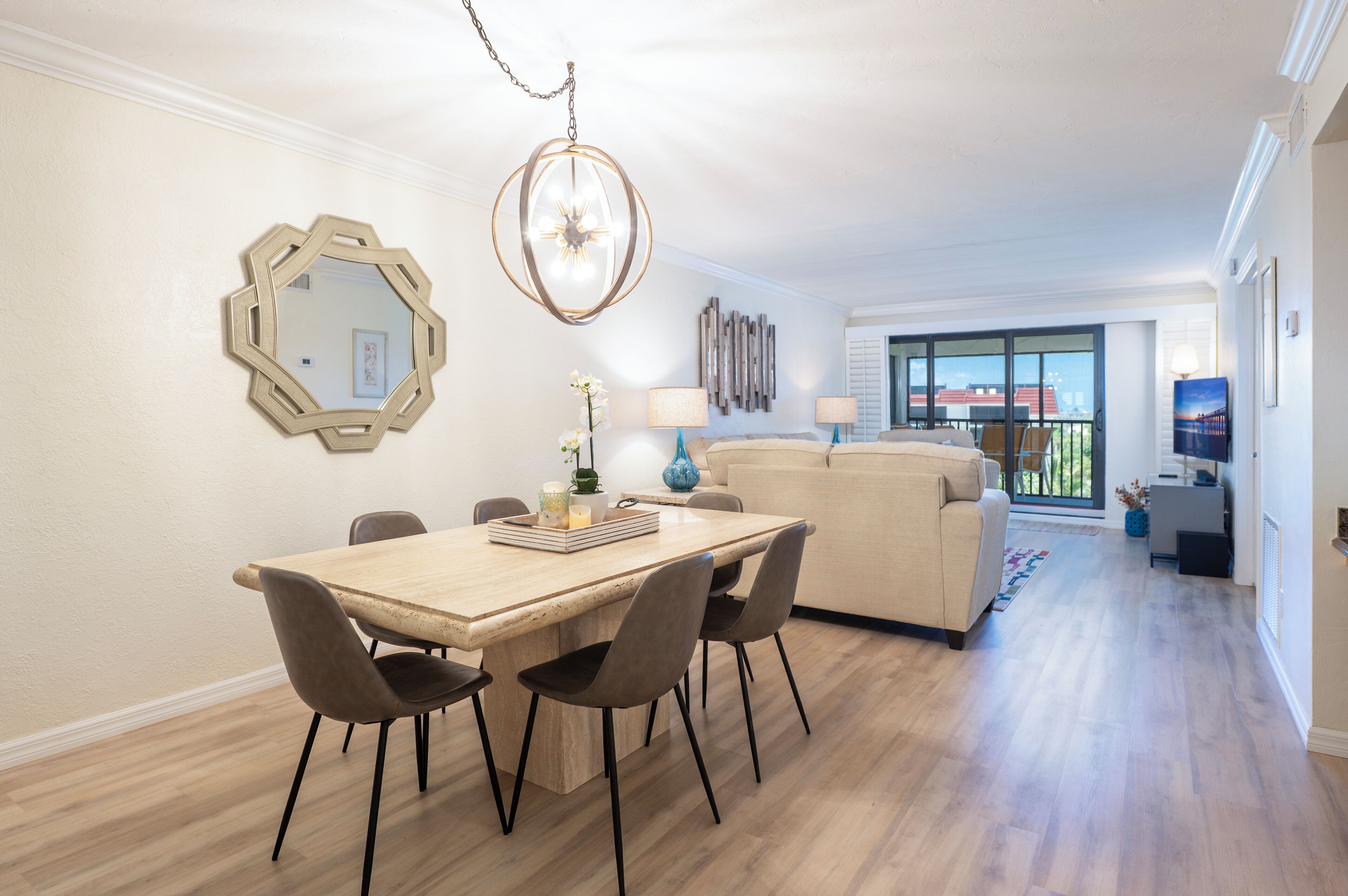 Un soggiorno moderno con un divano beige, un tavolo da pranzo in legno con quattro sedie, uno specchio decorativo e una lampada a sospensione.