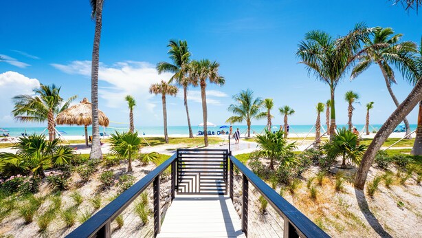 A wooden boardwalk leading to a beach with palm trees and a thatched umbrella. - Newly Renovated Penthouse  with Beautiful Views of the Gulf! (Sanibel)