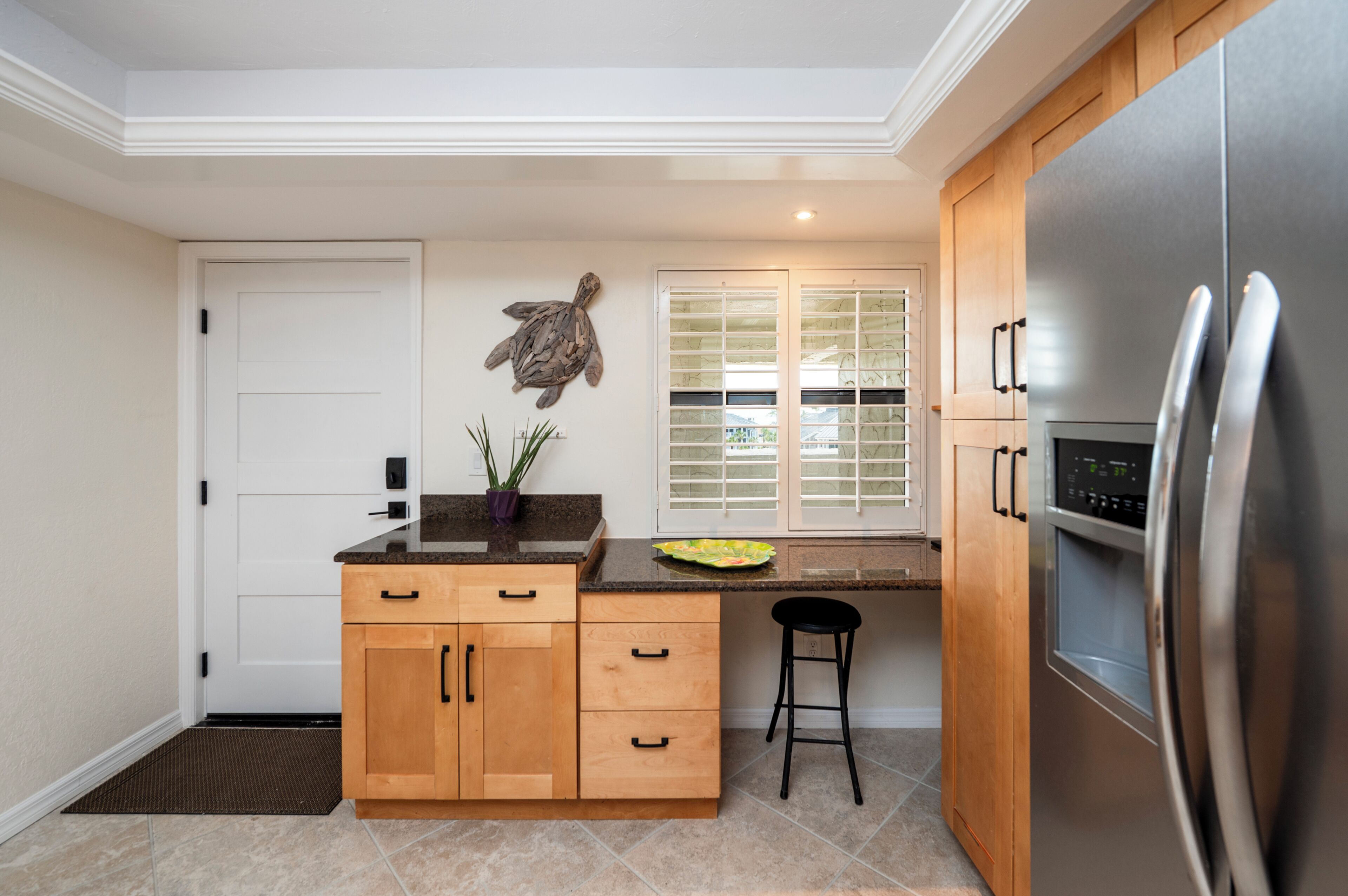 Una cocina con armarios de madera, un refrigerador de acero inoxidable, una planta en maceta y una ventana con persianas.