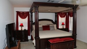 A four-poster bed with a canopy, a television on a stand, and a dresser with a mirror.