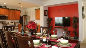 A dining area with a red accent wall, wooden cabinets, a flat-screen TV, and a dining table set with plates, glasses, and a bottle of wine.