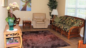 A living room with a beige armchair, a floral sofa, a dark rug, a green vase with flowers, and a tall plant. - Stunning 2BR Ranch, perfect for snowbirds or small families (Holiday)