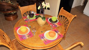 A round wooden dining table with four chairs, each with a woven backrest. The table is set with plates, bowls, and a vase with flowers. - Stunning 2BR Ranch, perfect for snowbirds or small families (Holiday)