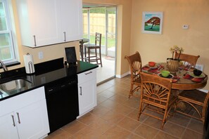 Une cuisine avec des meubles blancs, un plan de travail noir et un lave-vaisselle. On y trouve également un coin repas avec une table dressée pour deux personnes, des chaises et un vase rempli de fleurs.