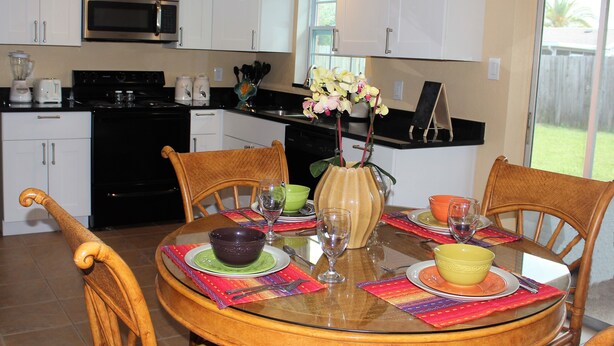 A modern kitchen with white cabinets, a microwave, and a dining area with a glass table set for four. - Stunning 2BR Ranch, perfect for snowbirds or small families (Holiday)