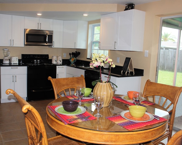 A modern kitchen with white cabinets, a microwave, and a dining area with a glass table set for four.