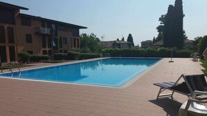 A swimming pool with a tiled deck, lounge chairs, and a building in the background. - Residence Don - pool, garden, 200m to the lake (Bardolino)