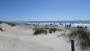 Une plage de sable avec une clôture en bois et des gens qui se détendent.