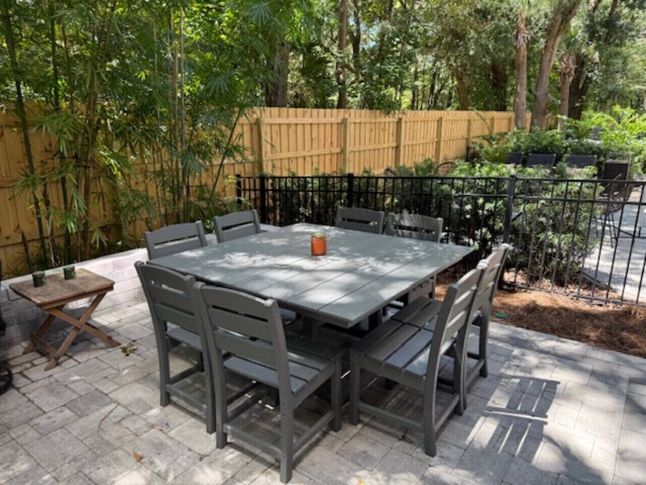 Une terrasse extérieure rectangulaire, avec une table et des chaises, entourée d’une clôture en bois et de verdure.