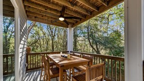 Une terrasse en bois, agrémentée d’une table et de chaises, entourée d’une rambarde et offrant une vue sur une zone boisée.