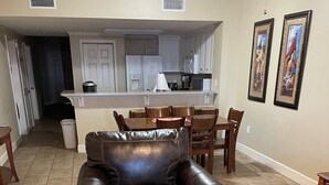 A living room with a leather armchair and ottoman, a dining area with wooden chairs, a kitchen with white cabinets, and a hallway leading to another room. - Family Beach Spot, Huge Balcony,4BR/3BA, 4 pools,top-notch exercise room, Tennis (Panama City Beach)