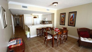 A dining area with a wooden table and chairs, a kitchen in the background, and two framed artworks on the wall. - Family Beach Spot, Huge Balcony,4BR/3BA, 4 pools,top-notch exercise room, Tennis (Panama City Beach)