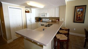 A kitchen with white cabinets, a large island with stools, a microwave, and a coffee maker. - Family Beach Spot, Huge Balcony,4BR/3BA, 4 pools,top-notch exercise room, Tennis (Panama City Beach)