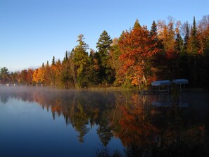 Una vista tranquilla su un lago, con foglie autunnali e un molo con posti a sedere coperti.