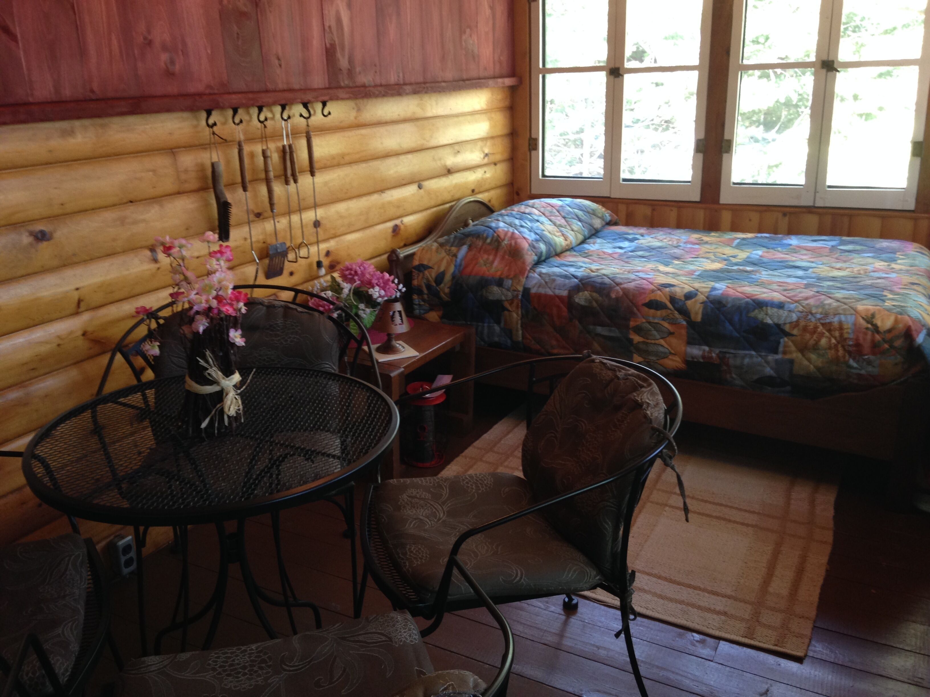 Una habitación de cabaña acogedora, con una cama, una mesa de comedor con sillas y una ventana con cortinas.