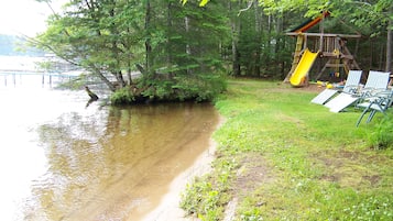 A lakeside scene with a playground, including a slide and swings, and a row of chairs facing the water.
