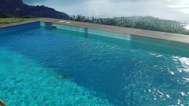 A clear blue pool with a wooden deck and a view of mountains and a lake. - Charming apartment with stunning views of Lake Como (Vestreno)