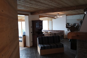 A cozy living room with a wooden ceiling, a sofa, a wooden cabinet, and a kitchen area in the background.