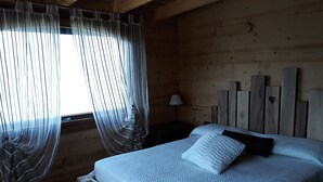 A wooden room with a bed, a window with sheer curtains, and a nightstand with a lamp. - Charming apartment with stunning views of Lake Como (Vestreno)