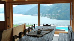 A wooden dining table with benches, a view of a lake and mountains, and a wooden ceiling. - Charming apartment with stunning views of Lake Como (Vestreno)