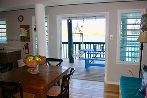 A dining area with a wooden table and chairs, a hanging light fixture, and a view of the outside deck.