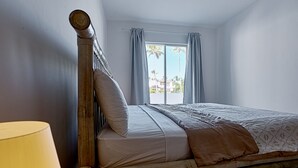 A bed with a wooden headboard, a bedside lamp, and a window with curtains. - Los Corales Beach Village - Your private paradise - 2BR first floor - LT#B2 (Punta Cana)
