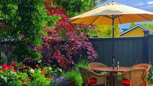 An outdoor patio with wicker chairs and a table, surrounded by a variety of colorful flowers and plants. - Titania - Second Spring Property 1-3 Bedroom Luxury Rentals In Downtown Ashland (Ashland)