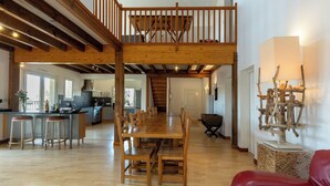 A spacious kitchen with a wooden dining table and bar stools, a staircase leading to an upper level, and a rustic decor piece on the wall. - 4* Gallery Villa in Moliets, 15 p, heated pool, ensuite rooms/ close 2 beach (Moliets-Et-Maa)