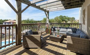 Una terraza de madera con mobiliario de mimbre, una piscina y vistas a una zona residencial.