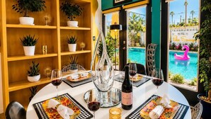 Un coin repas avec vue sur la piscine, une table dressée avec des verres à vin, des assiettes et un plateau de fruits.