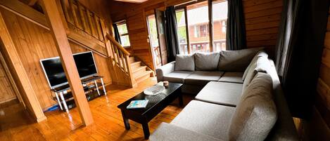 A wooden interior with a sofa, TV, and staircase.