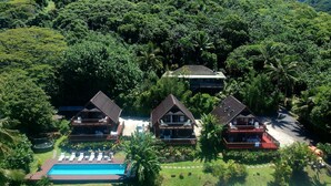 Um resort com três cabanas de madeira, uma piscina e vegetação exuberante.