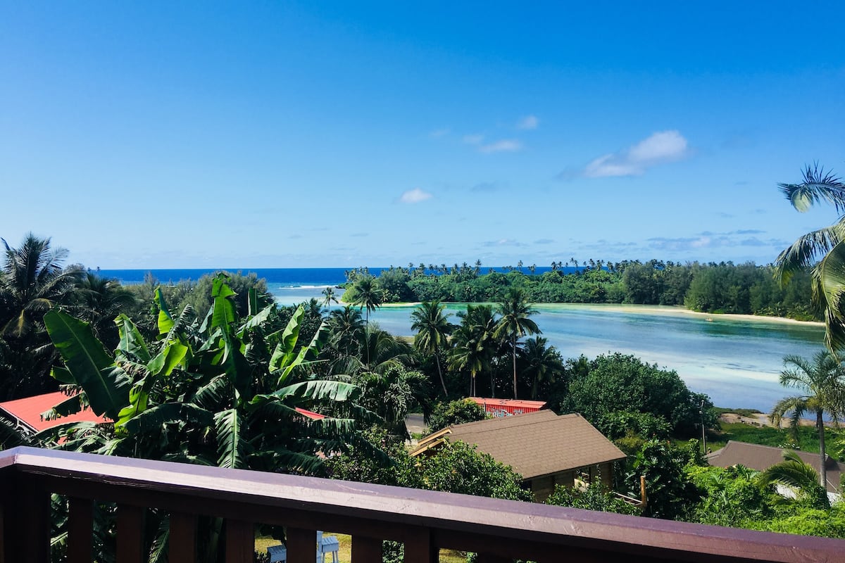 A tropical landscape with a clear view of a beach and ocean, surrounded by lush greenery and palm trees.