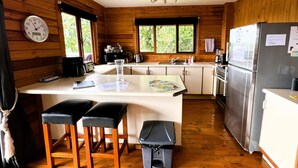 Uma cozinha estilo cabana, com paredes de madeira, uma ilha central com bancos, geladeira e um relógio na parede.