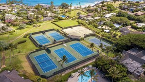 Ett flygbildsbild av ett bostadsområde med flera tennisbanor, en swimmingpool och en strand i bakgrunden.