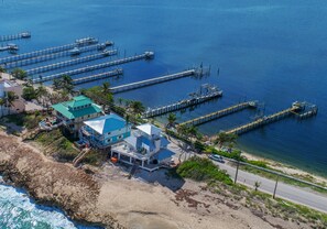 An aerial view of a coastal property with a large house, multiple docks, and a beach.
