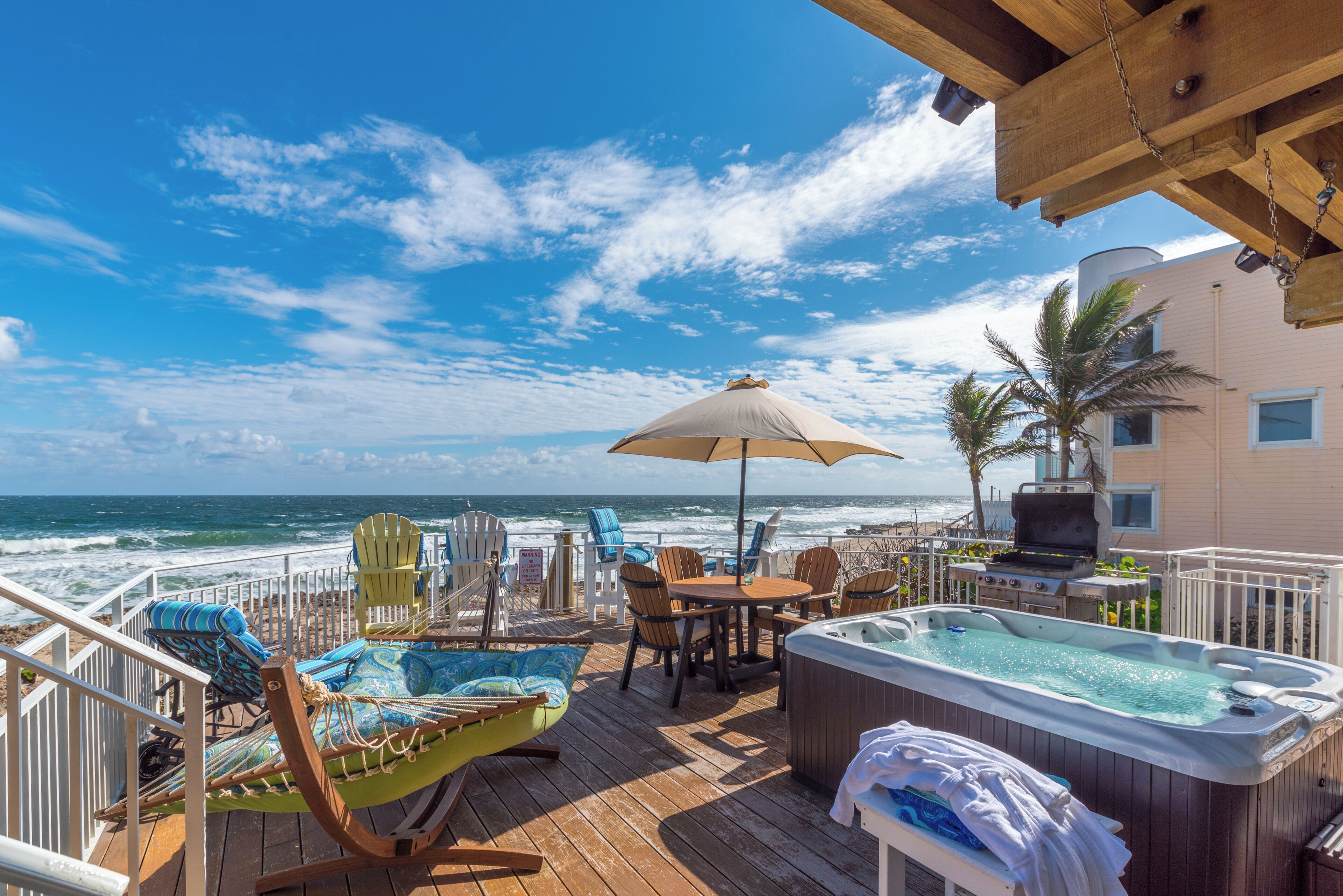 A deck with a view of the ocean, outdoor seating, and a hot tub.