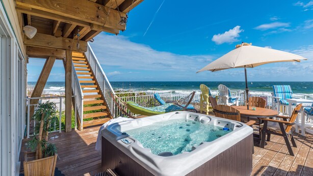 Une terrasse en bois avec un jacuzzi, un espace salon extérieur et une vue sur l’océan.