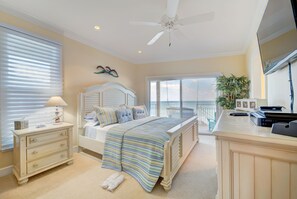 A bedroom with a bed, dresser, lamp, and a view of the ocean through large windows.
