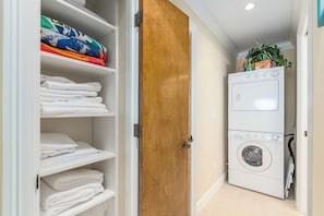 A laundry room with a stacked washer and dryer, a wooden door, and shelves with folded towels.