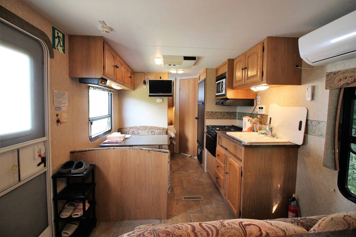 A compact RV kitchen with wooden cabinets, a stove, microwave, and a small dining area.